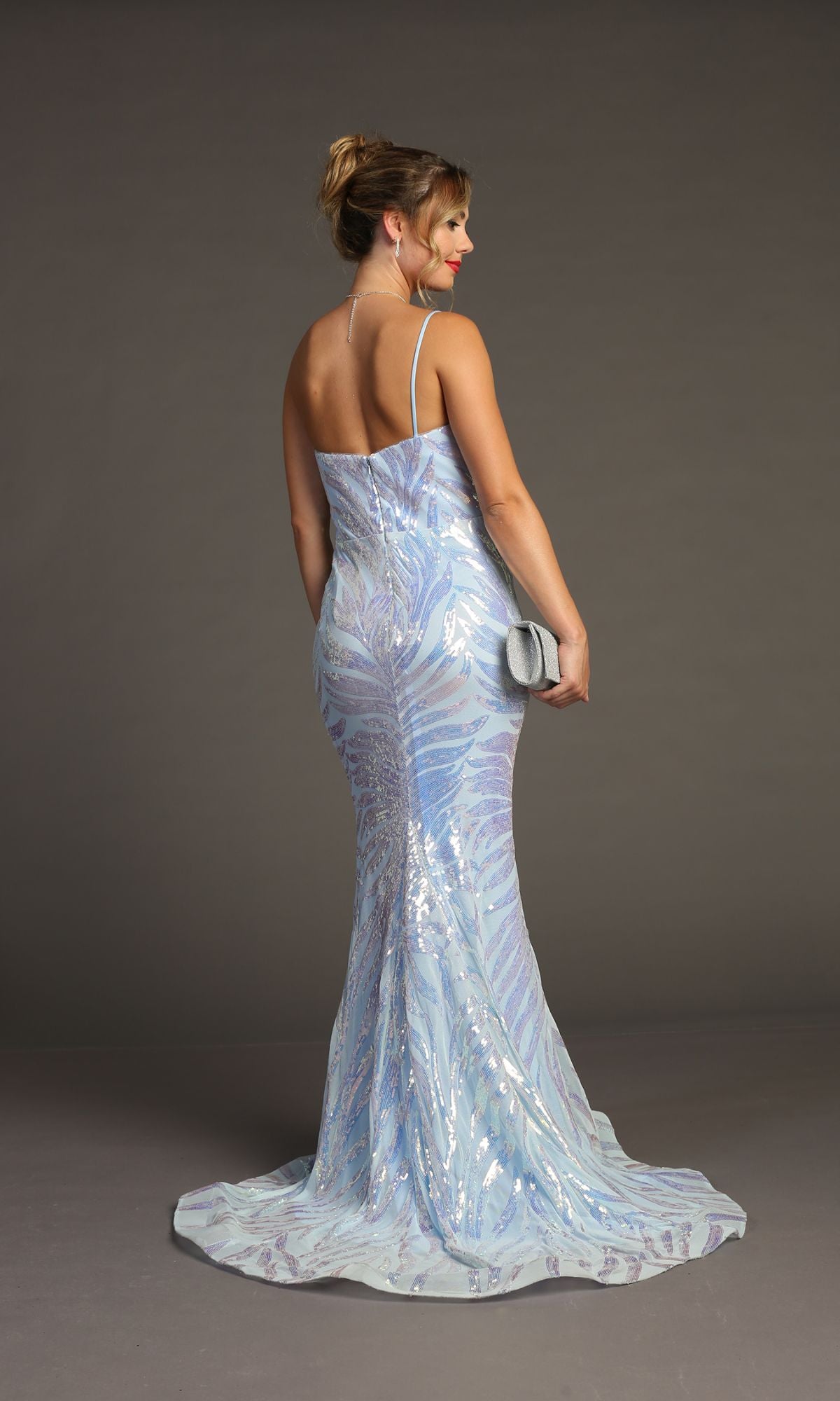 Woman in the Sequin-Print One-Shoulder Prom Dress: Chicas C823, a light blue floor-length gown, holding a silver clutch and posing against a plain gray background.